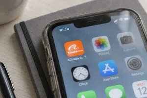 Close-up of the Alibaba.com app icon on a smartphone resting on a notebook.